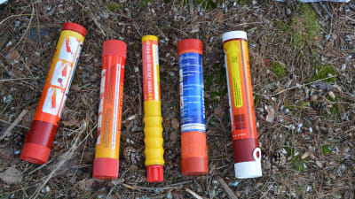 Fem nödraketer i rött, orange och gult ligger på en barrig stig.