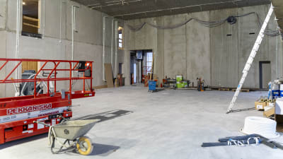 Byggmaterial och redskap står i en stor sal med betongväggar.