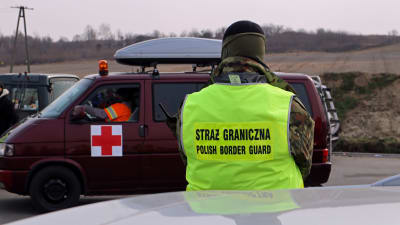 En man i neongul väst från polska gränsbevakningen tittar på en minibuss som markerats med ett rött kors.