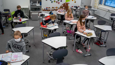 En skolklass med andraklassare sitter vid sina pulpeter. Alla har munskydd.