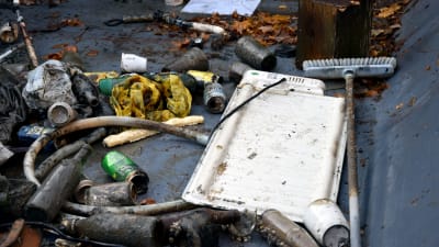 Leriga flaskor, en plastslang, en sopborste och ett värmeelement ligger i en container.