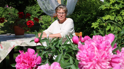 Margareta "Teta" Reinlund sitter i trädgårdens pergola och njuter av blommande pion