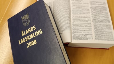 Ålands lagsamling 2008, en blå bok med guldtext på pärmen, ligger på ett brunt bord.