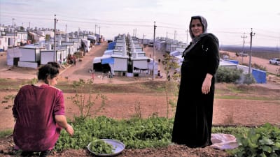 Två kvinnor på en kulle framför ett flyktingläger i norra Irak