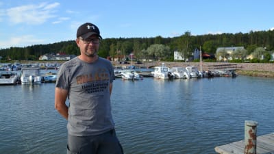 En man står på en brygga med flera bryggor med båtar i bakgrunden.