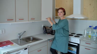 En kvinna står i ett kök och öppnar två köksskåpsdörrar. 