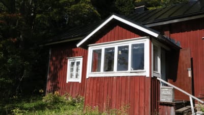 Ett rött stockhus med en veranda med stora glasfönster. 