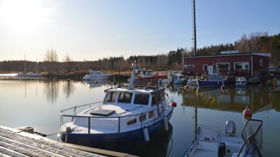 Några båtar som ligger vid Isnäs hamn på hösten då det redan ligger lite snö på bryggan. Vattnet är stilla och solen skiner.