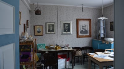 Ett rum med tavlor på några av Finlands presidenter på väggarna. På flera bord i rummet finns lösöre som är till salu på loppis.