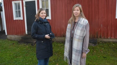 Två kvinnor står framför ett rött hus.