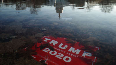 En röd skylt med texten Trump 2020 Make America Great har hamnat bland döda löv i en vattenpöl.