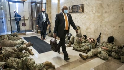 Bild på soldater som sover i USA:s kongressbyggnad och en kostymklädd man går i mitten.