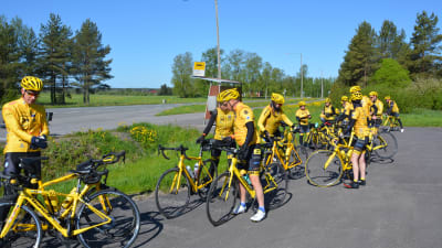 En grupp cyklister i gula dräkter har tagit paus vid en busshållplats.