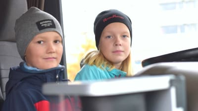 Två barn, en flicka och en pojke, sitter i förarhytten på en lastbil.