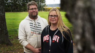 Patrik och Lotten Eklund står bredvid varandra på sin gård i Kimito. De tittar in i kameran med rätt allvarliga miner. I förgrunden en björkstam.