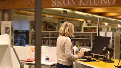 En kvinna med ljust hår vid desken på ett bibliotek.