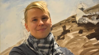 Ung man poserar framför en tavla.
