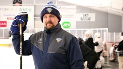 Jan-Peter Lassila, målvaktstränare i hockeyföreningen MUIK i Nykarleby, står med hockeyklubban invid sargen, redo att inleda kvällens träning.  