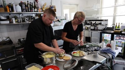 Två svartklädda personer lägger upp mat i ett restaurangkök