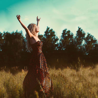 Nuori nainen pellolla kasvot kohti valoa kädet ojennettuna ylöspäin.