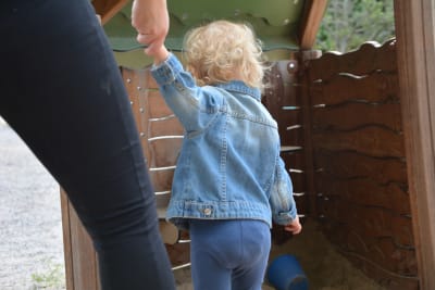 En mamma håller i handen på sitt barn som har en jeansjacka på sig.