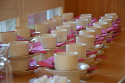 Flera kaffekoppar står uppradade med rosa servetter. 