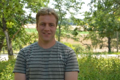 En blond man med randig t-skjorta ser in i kameran.