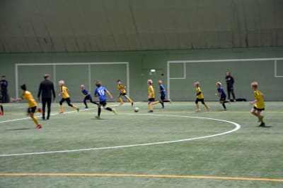 Fotbollsspelare från åifk p11-laget och FC Inter spelar fotboll på en fotbollsplan inomhus.