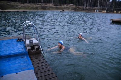 Två kvinnor i mössa simmar mot brygga