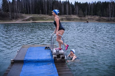 En kvinna står på stege vid en brygga och den andra simmar mot bryggan