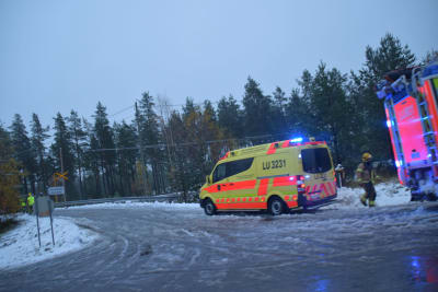 En ambulans står vid en snöig plankorsning. På bilden syns också flera brandmän.