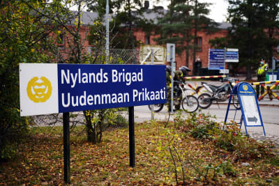 En skylt där det står Nylands brigad på svenska och finska. I bakgrunden syns porten till garnisonsområdet.