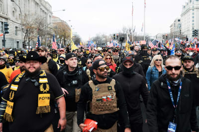 Suuri joukko Trumpin kannattajia marssii kadulla, Etualalla on pääosin mustiin pukeutunutta väkeä. Keskellä on Proud Boys -järjestön johtaja, parrakas Enrique Tarrio mustissa laseissa ja lippalakissa, jonka lippa on käännetty niskan puolelle.