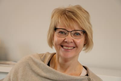 En kvinna med kort blont hår och glasögon skrattar.