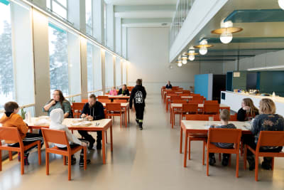 Paimion parantolan ruokasalissa. Plydissä on perheitä ruokailemassa ja kaukana tilan takaosassa istuu arkkitehti Henna Helander.