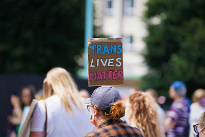 En person demonstrerar och håller i en skylt där det står "trans lives matter".
