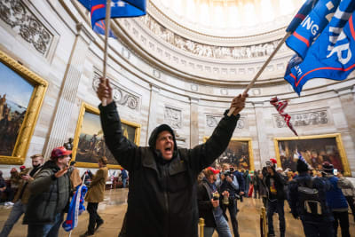 En man viftar med en flagga inne på Capitolium efter stormningen 6.1.2021.