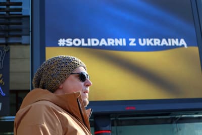 En man står framför en skylt i blågult som uppmanar till solidaritet med Ukraina.