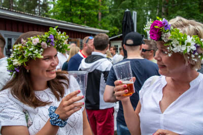 Två kvinnor med blomkransar på huvudet skålar.