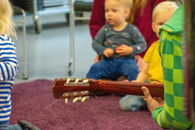 Bild på en gitarr med barn från en musiklekskola i bakgrunden.