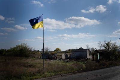 En ukrainska flagga vajar frqamför ett sönderbombat hus