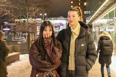 Två unga kvinnor i stadsmiljö, den ena håller handen över halva ansiktet. 