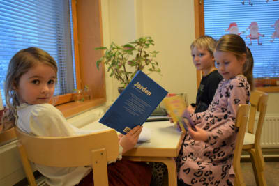 Tre elever i förskolan bläddrar i böcker vid ett bord. Det är två flickor och en pojke på bilden.