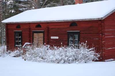 En gammal röd träbyggnad i ett vinterlandskap.