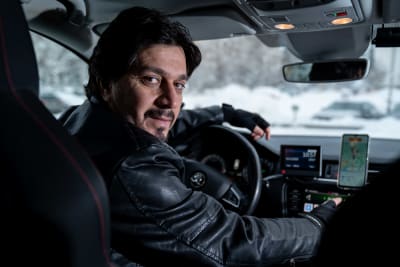 Taxichauffören Barzan Namiq i svart läderrock sitter i sin bil.