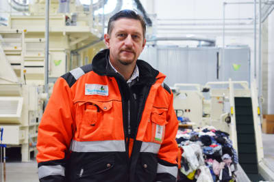 En brunhårig man med orange-svart rock ser in i kameran.