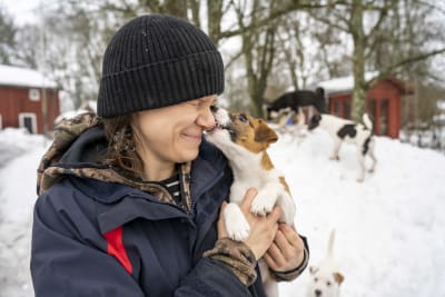En kvinna med en valp i famnen. Valpen slickar henne i ansiktet. 