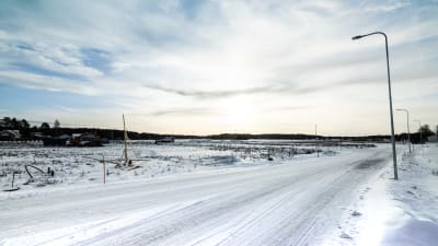 Snöig väg som leder ut till obebyggt bostadsområde
