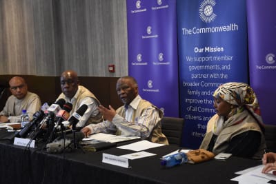 Fyra personer sitter bakom ett långt bord. Vid en plats finns det många mikrofoner. Där sitter Thabo Mbeki. Bakom honom syns Samväldets logotyp och texten The Commonwealth.