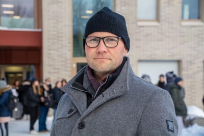 Sebastian Lindqvist vid ingång till byggnad. Utanför byggnaden står människor i klungor. 